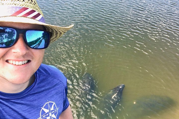 a person wearing a hat and sunglasses in front of a body of water