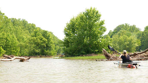 a man riding on the back of a boat next to a river