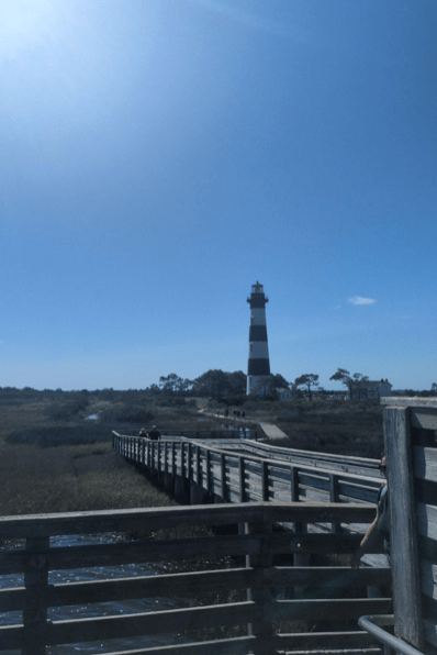 Striped lighthouse and wooden walkway under clear blue sky.