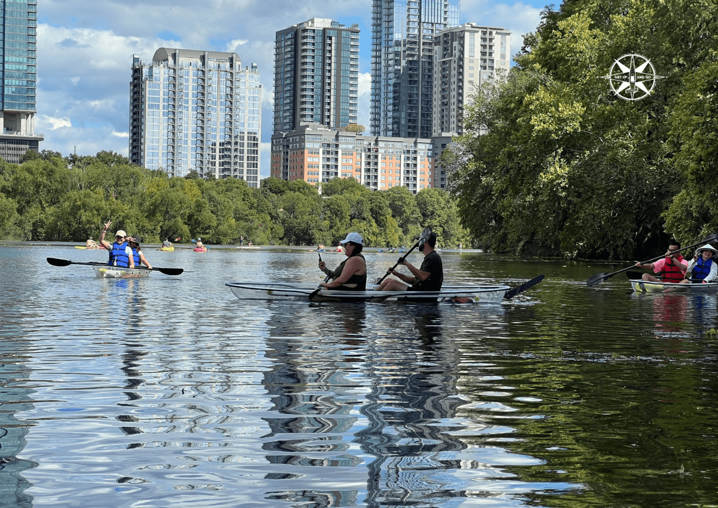 People kayaking on a river with city skyscrapers in the background.
