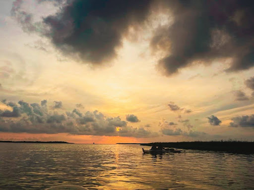 Kayakers on a calm lake at sunset with dramatic clouds overhead.