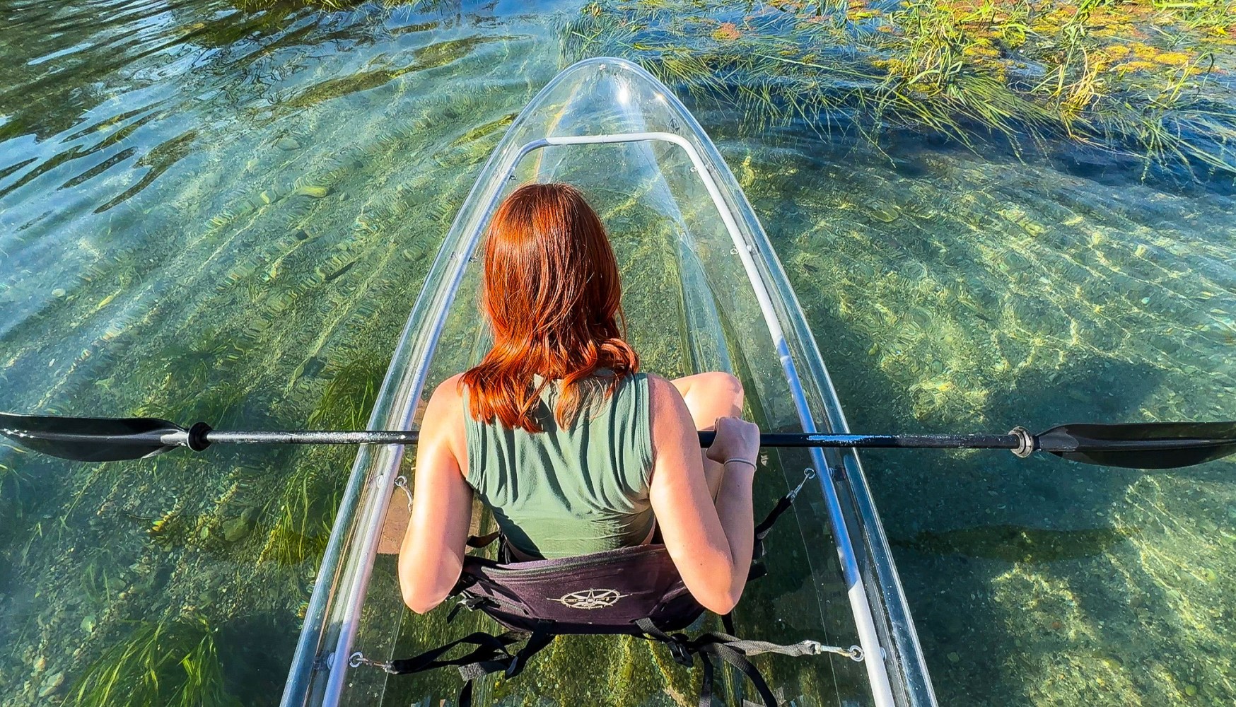 Person kayaking in clear waters with a transparent kayak, view from above.