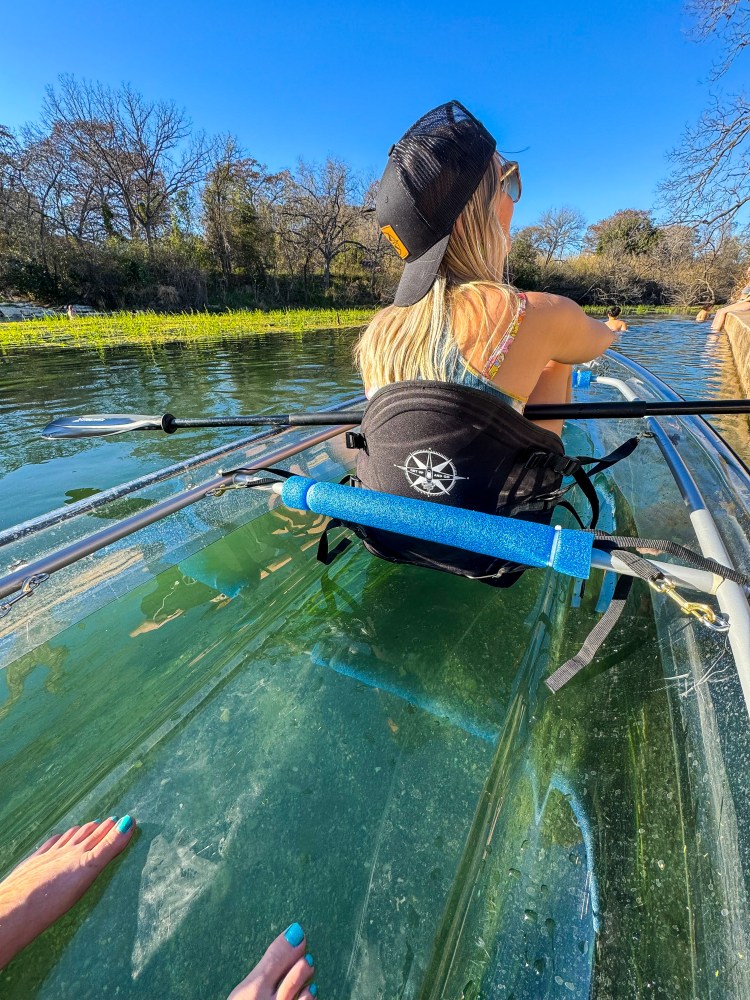 Person kayaking on clear water with trees and blue sky in the background.