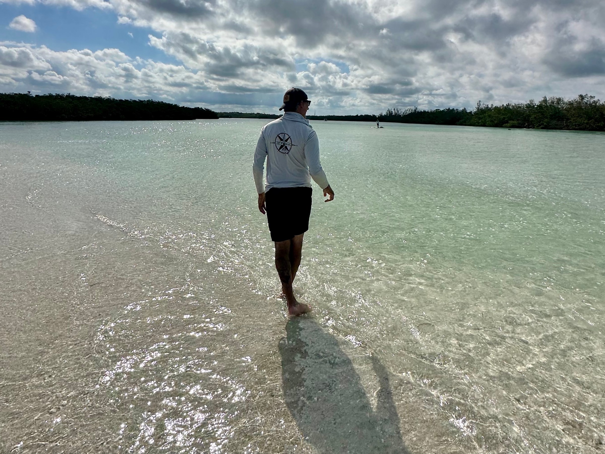 Person walking through clear shallow water under a cloudy sky.