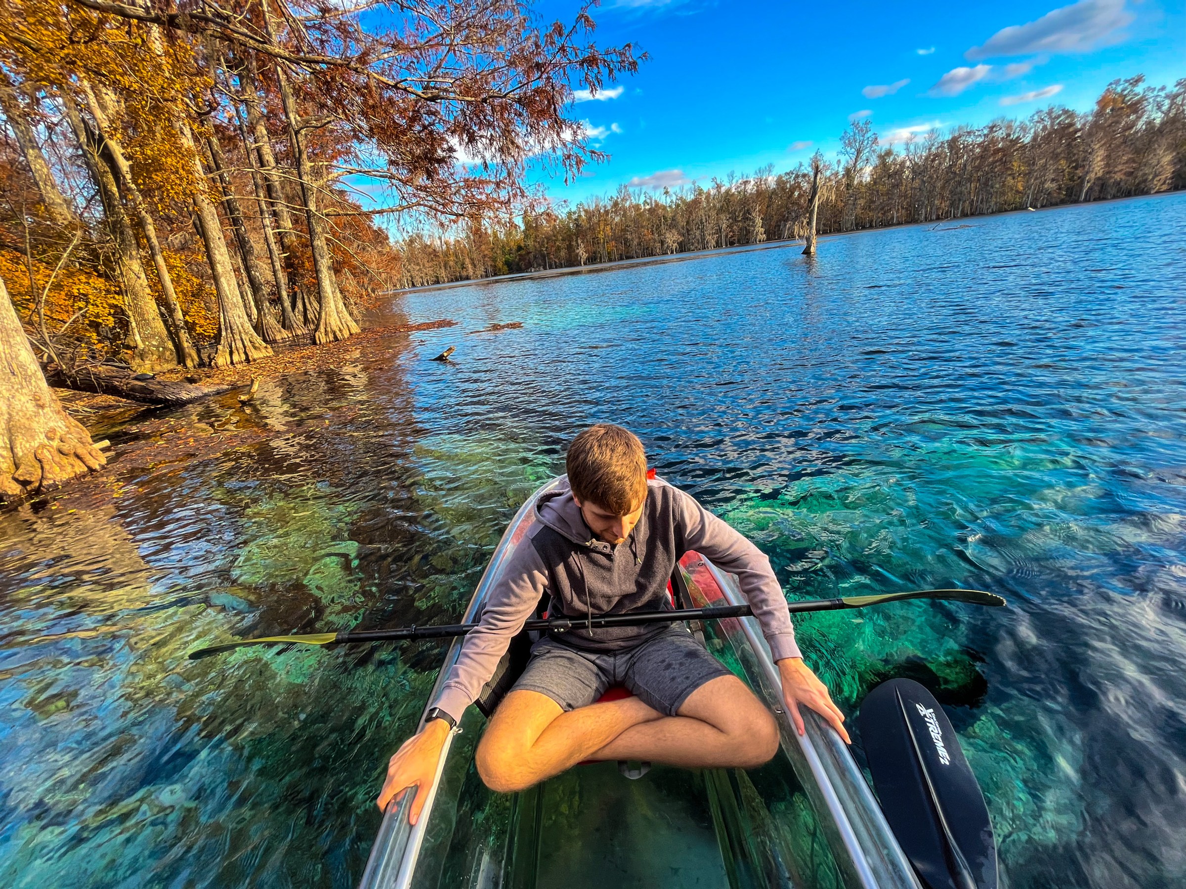 Kayak in lake Person sitting in a clear kayak on a calm lake surrounded by trees in autumn.