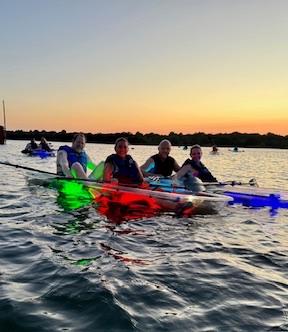 highres_page1_0 Four kayakers on a calm lake at sunset, with colorful lights in their kayaks.