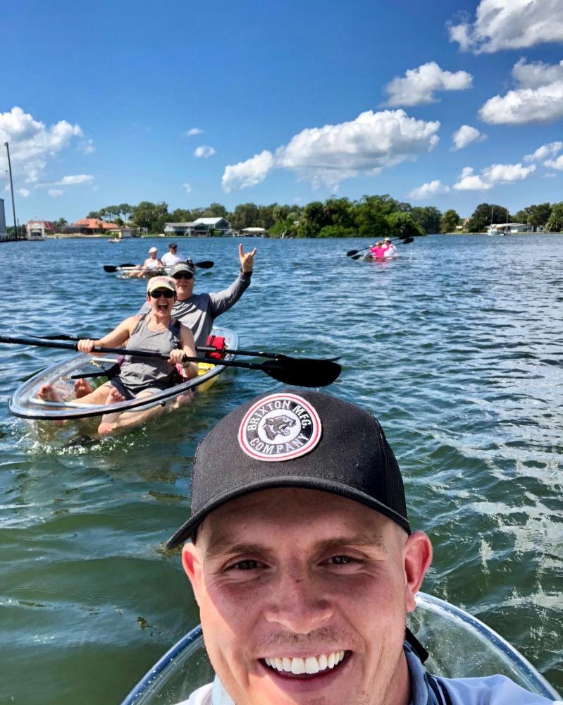 Group kayaking in clear kayaks on a sunny lake, smiling and enjoying the day.