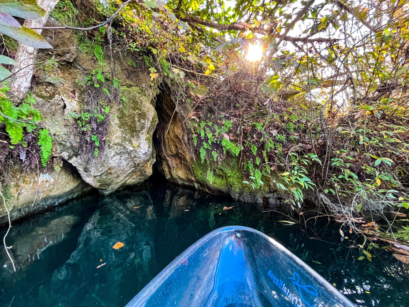 Blue kayak on a clear waterway near rocky shore with foliage.