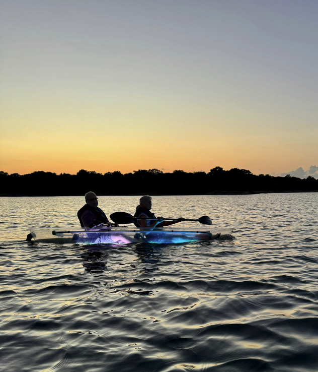 Two people kayaking at sunset with glowing lights under their kayak.