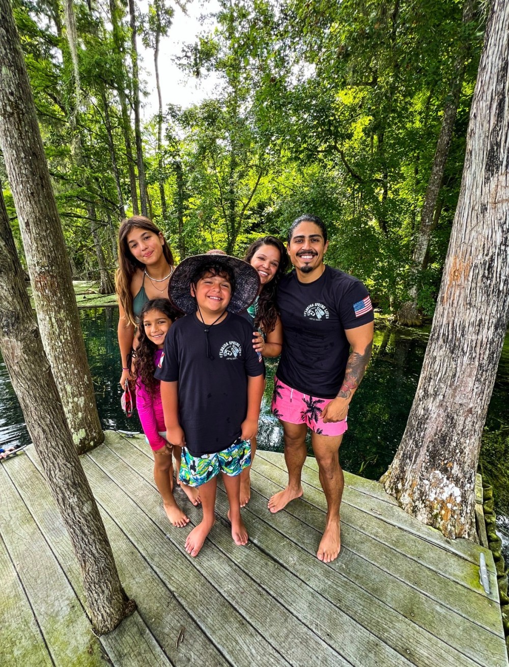 Group of five people smiling on a wooden deck in a forested area.