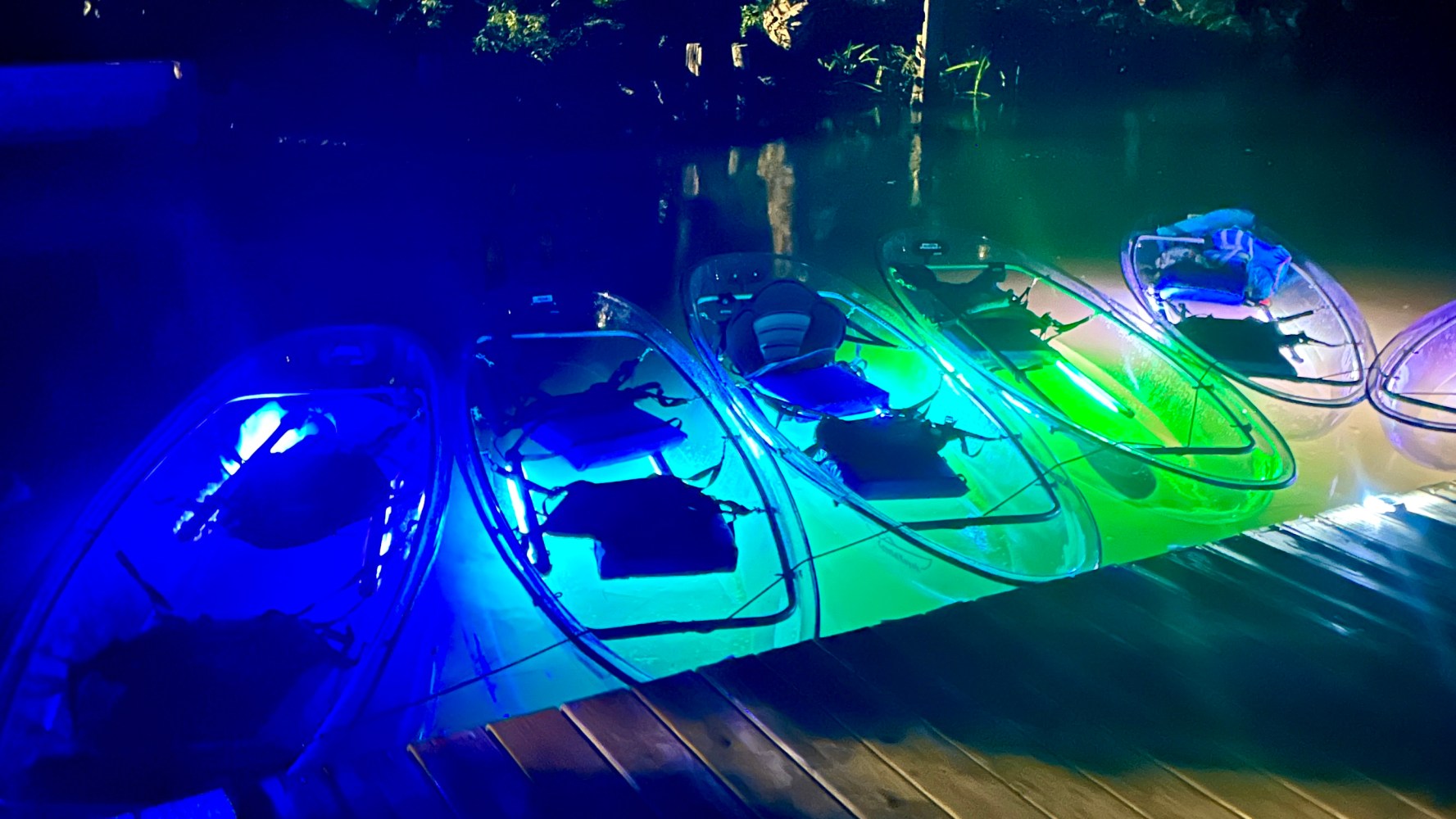 Illuminated clear kayaks with colorful LED lights docked at night.