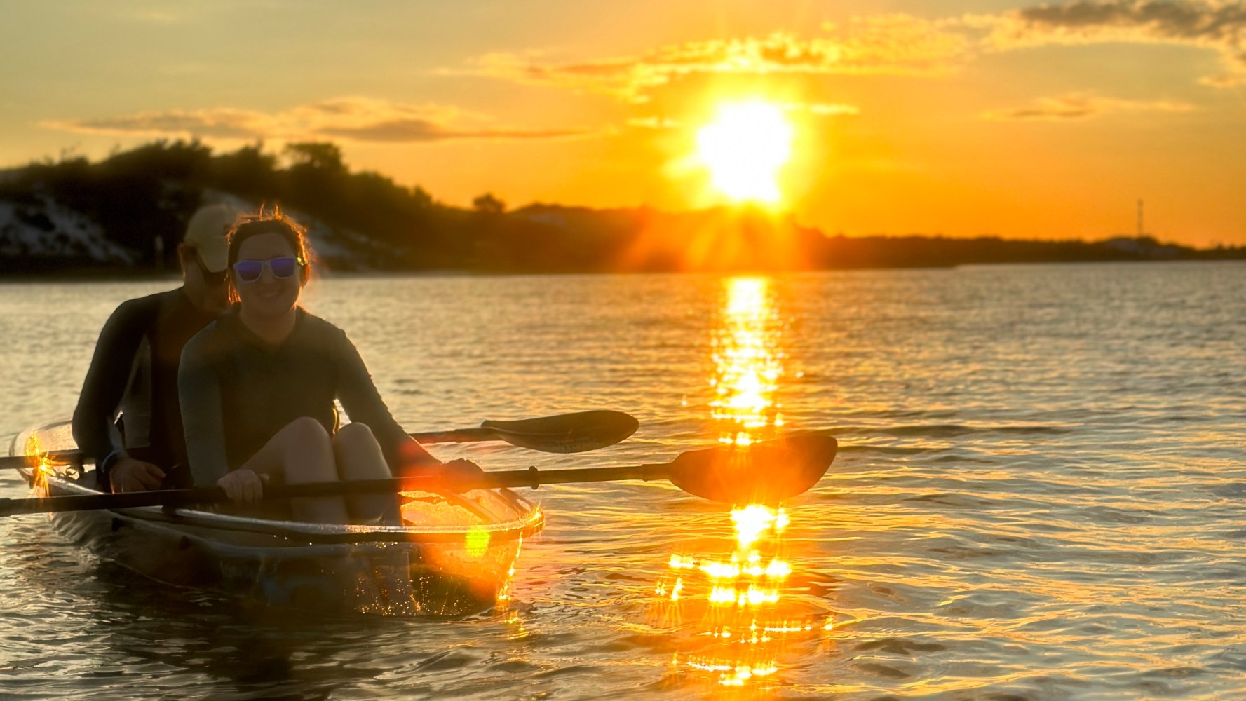 Two people kayaking on a lake during a golden sunset.