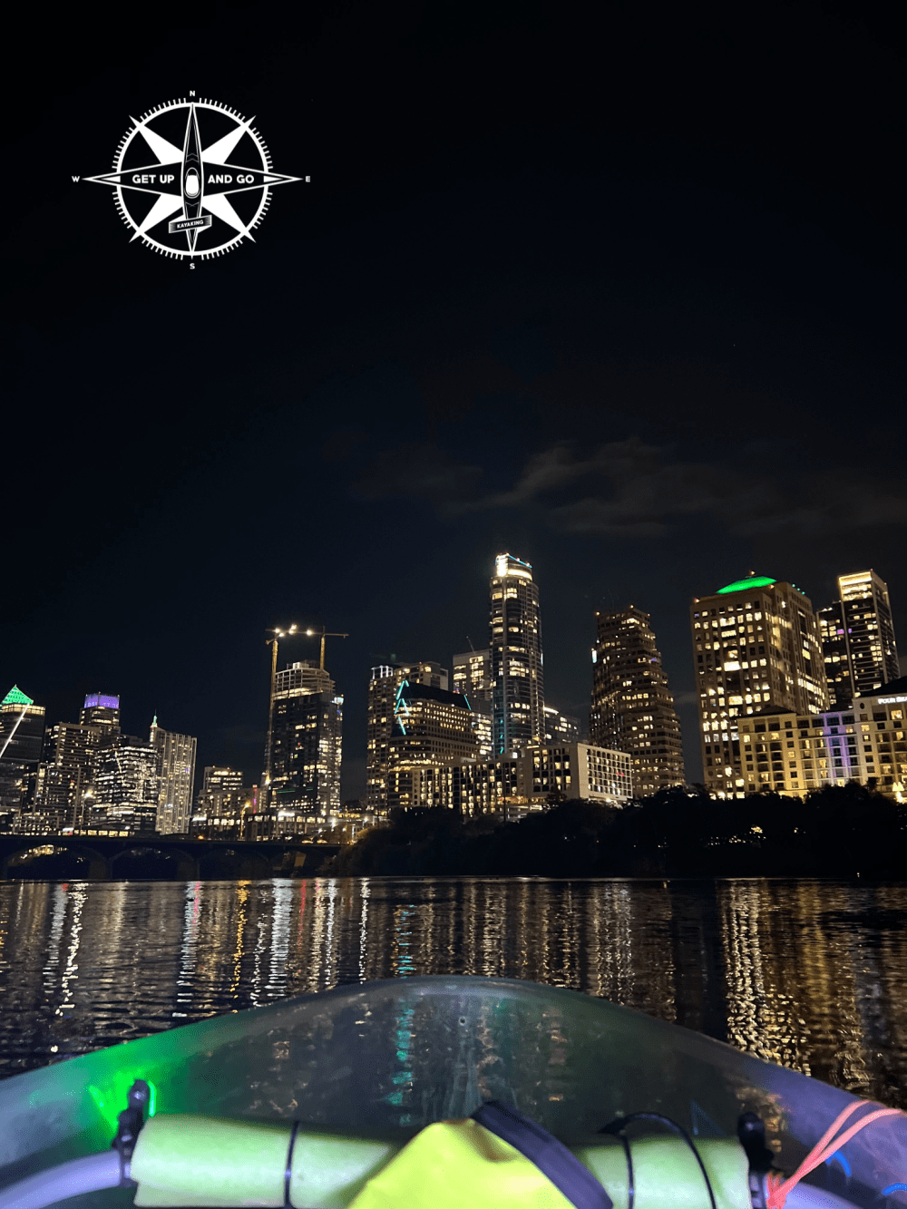 City skyline at night with river reflection and compass logo in corner.