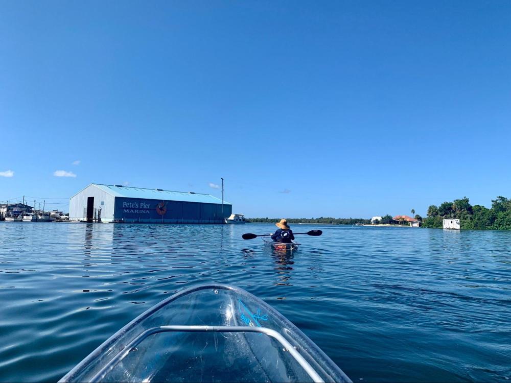 Person kayaking on calm water near Pete's Pier Marina under a clear blue sky.
