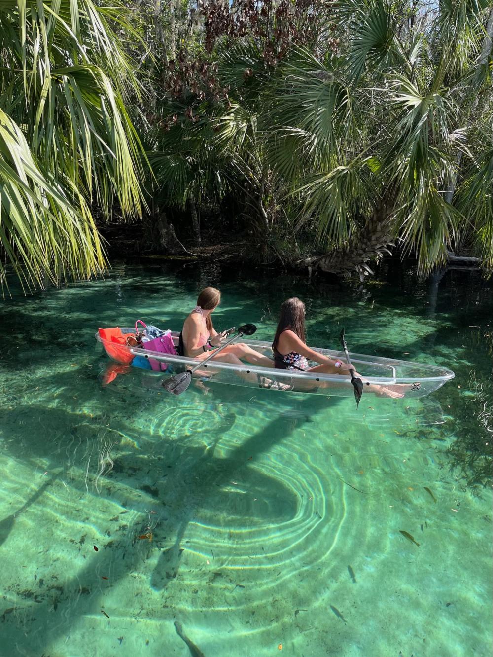 Two people canoeing in a clear kayak on a tropical jungle river.