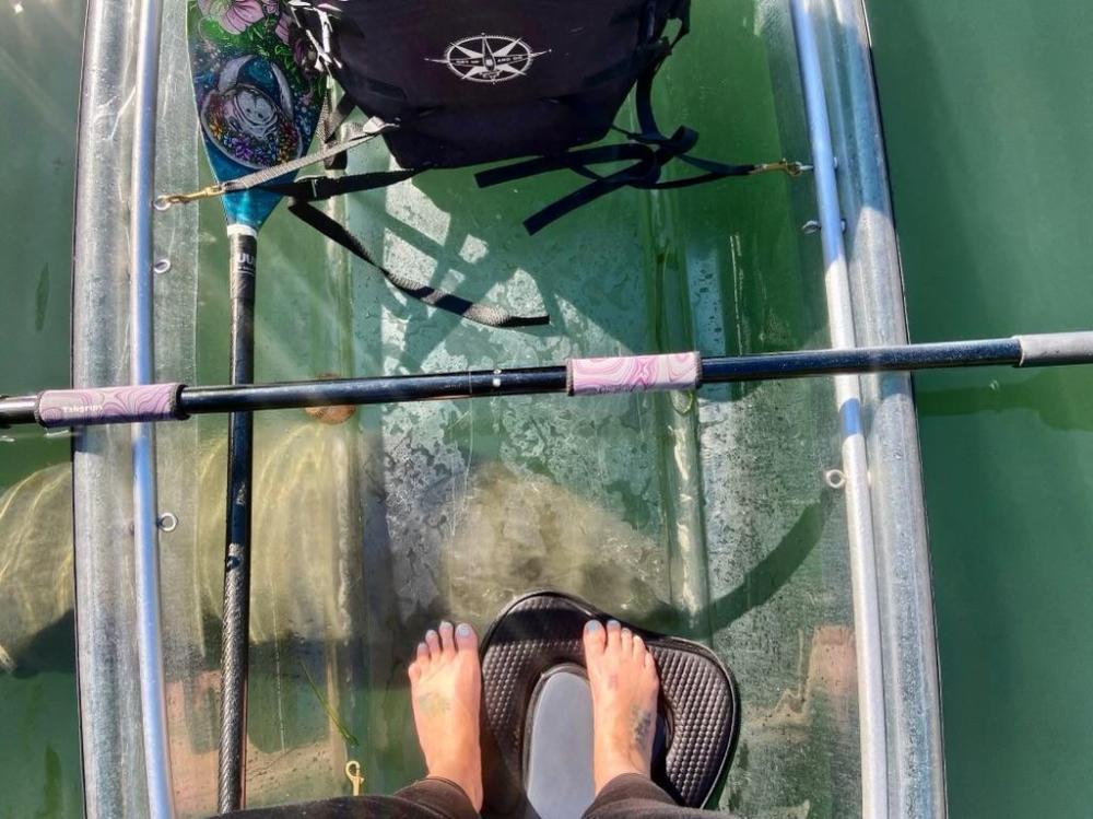 View inside a transparent kayak with a paddle and bare feet visible.