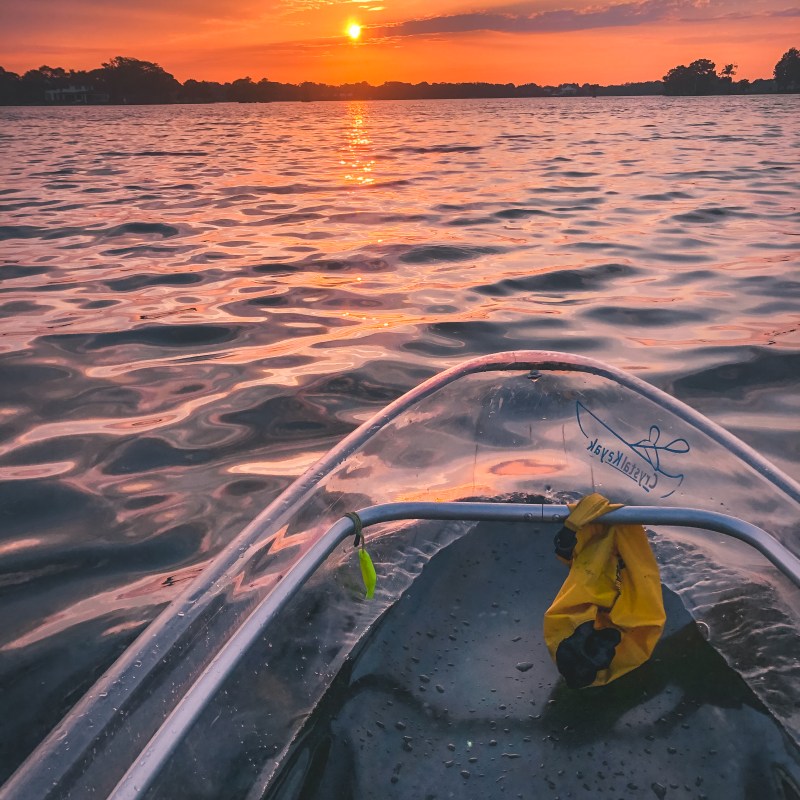 Clear kayak on a lake during a vibrant sunset with orange and pink hues.
