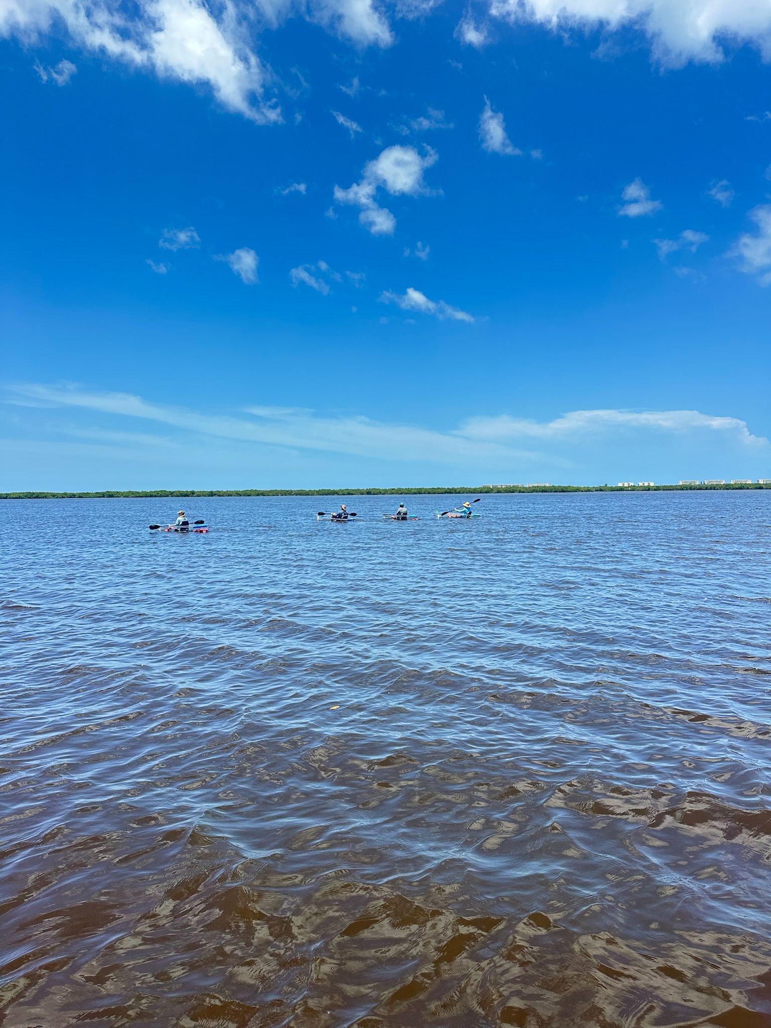 People kayaking on a wide expanse of water under a clear blue sky with clouds.
