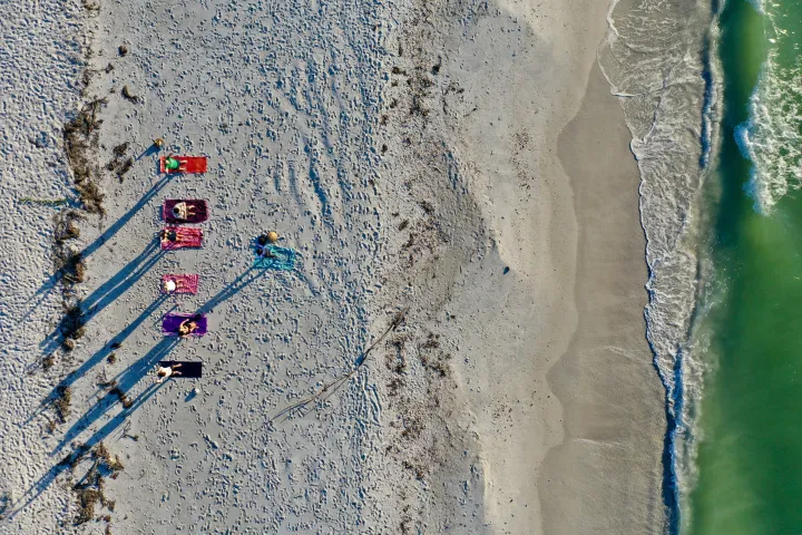 Aerial view of six people sunbathing on a sandy beach near the ocean waves.