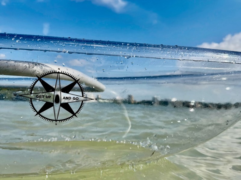 Transparent kayak with compass design on water under blue sky.