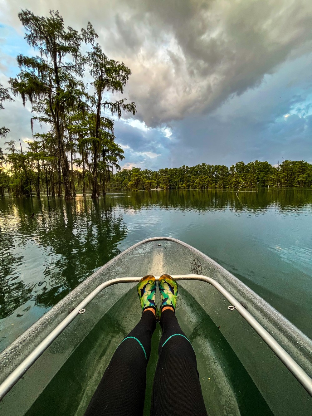 Feet in kayak on calm lake with trees and cloudy sky in background.