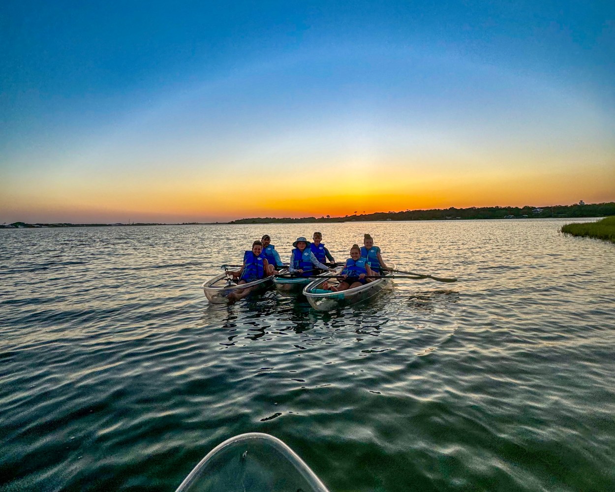 Group kayaking at sunset on a calm lake, with five people in two canoes.