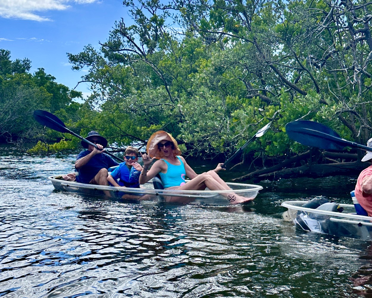 Three people kayaking on a river surrounded by lush green vegetation.