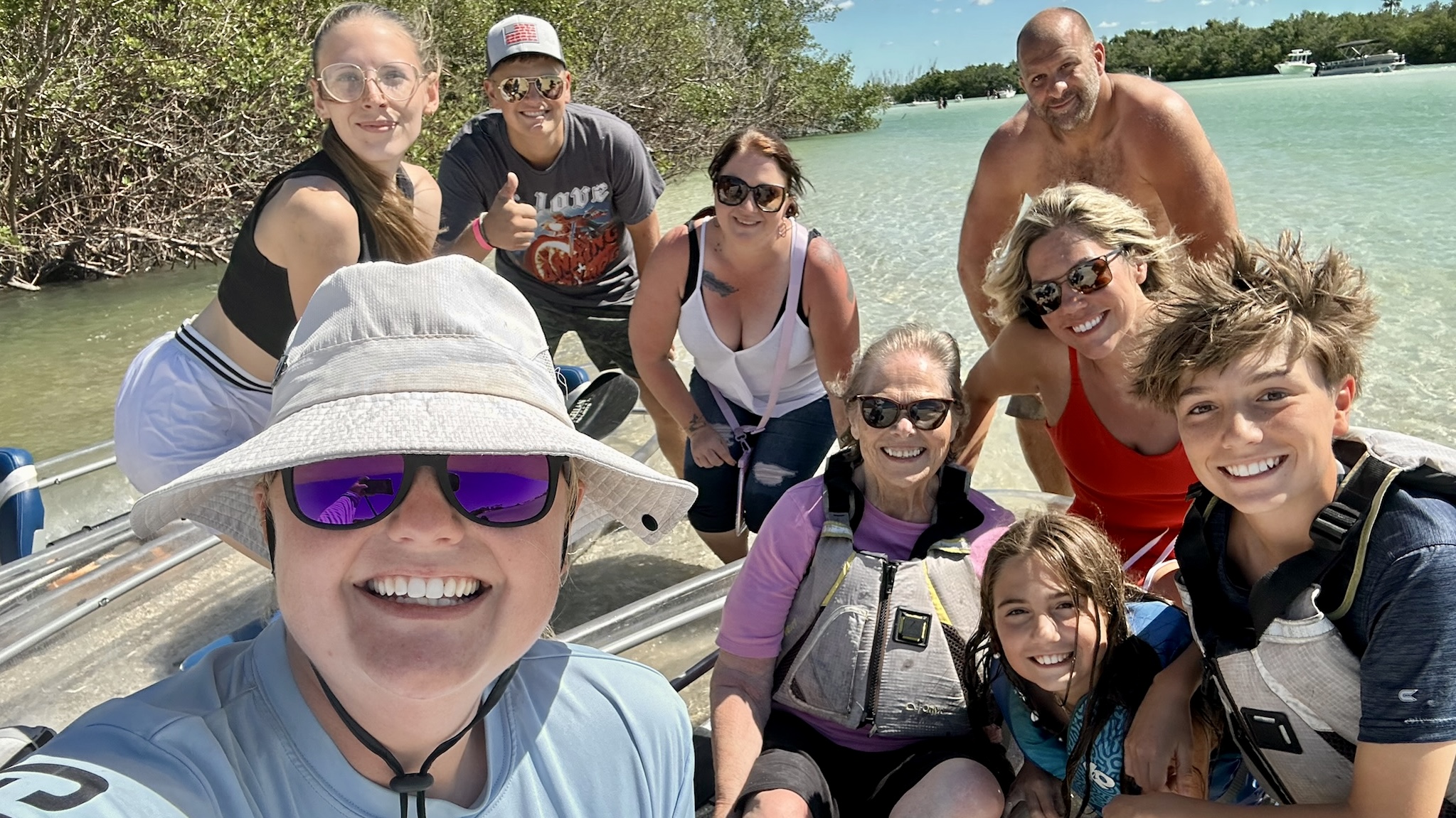 Group of eight people smiling on a boat by the water with clear skies.