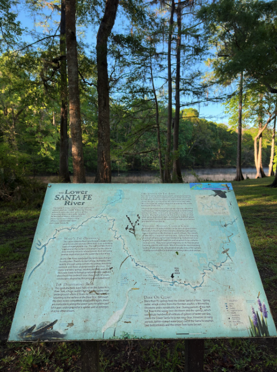 Informational sign about the Lower Santa Fe River in a wooded area by the river.