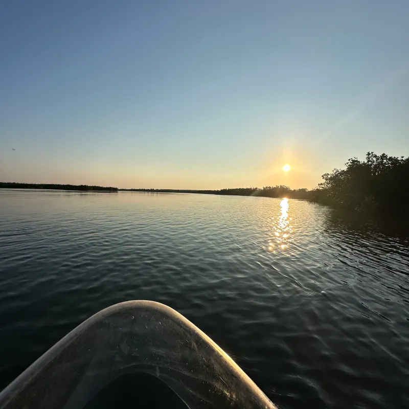 Sunset over calm lake from the bow of a boat with clear sky.