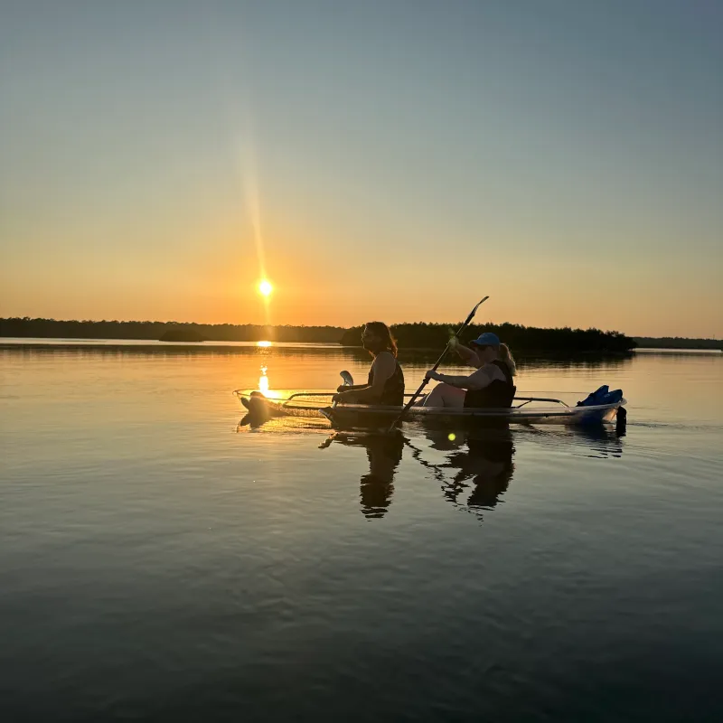 Two people kayaking on a lake at sunset with calm water.