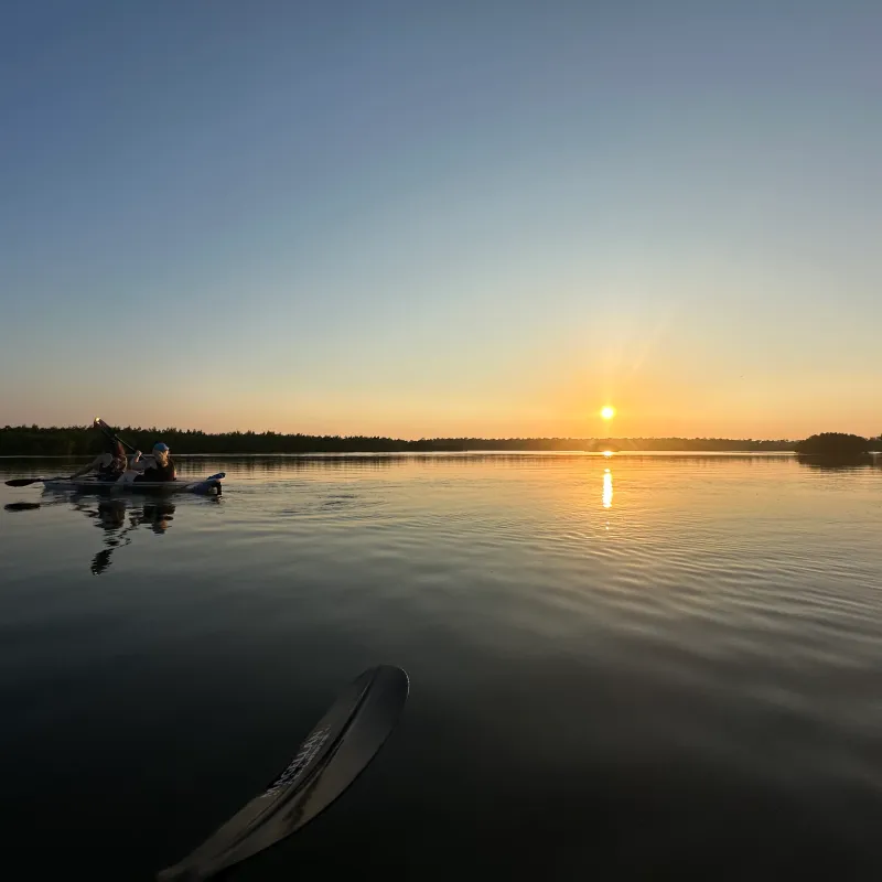 Two people kayaking on a calm lake at sunset with clear skies.