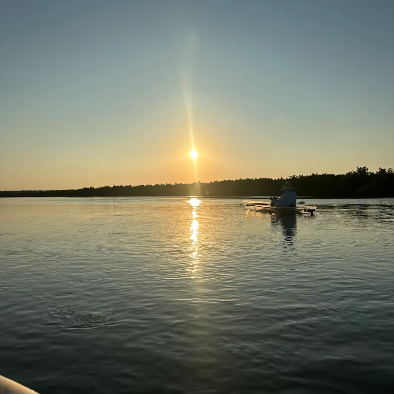 Sunset over a calm lake with a single boat silhouetted against the horizon.