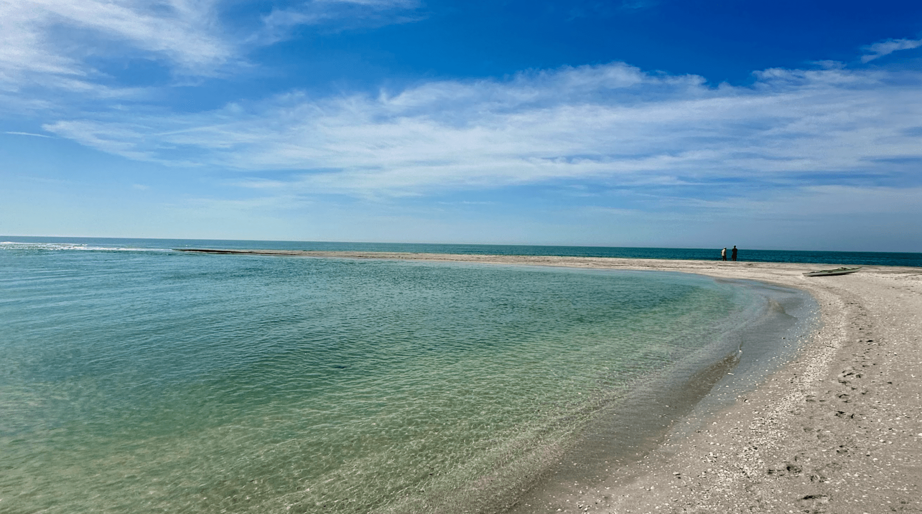A tranquil beach with clear blue water and a distant horizon under a partly cloudy sky.