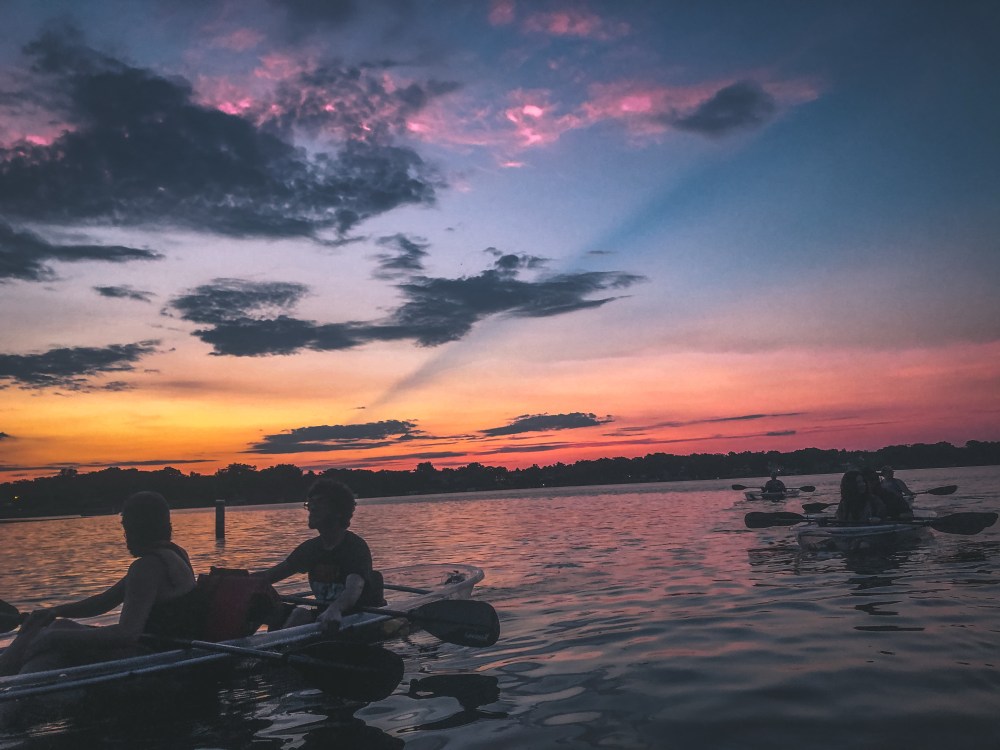 People kayaking on a lake during a vibrant sunset with colorful skies and clouds.
