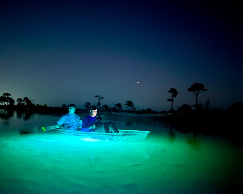 Two people boating at night in a glowing kayak on a calm lake.