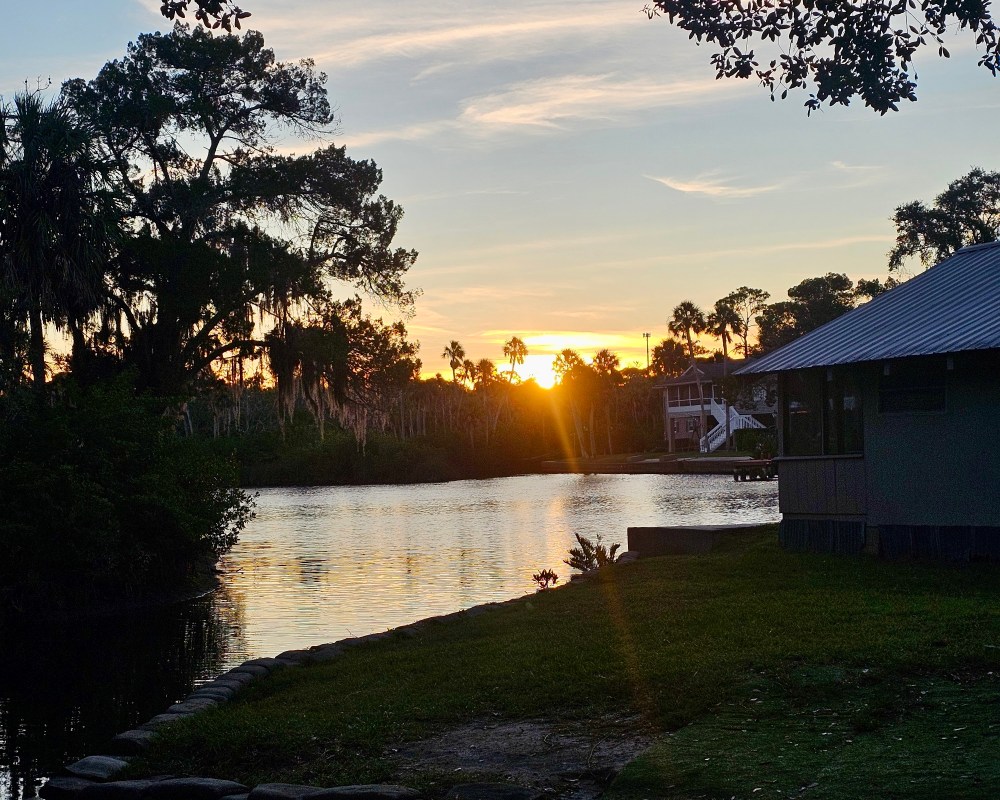 Sunset over a river, trees silhouetted, house on the right.