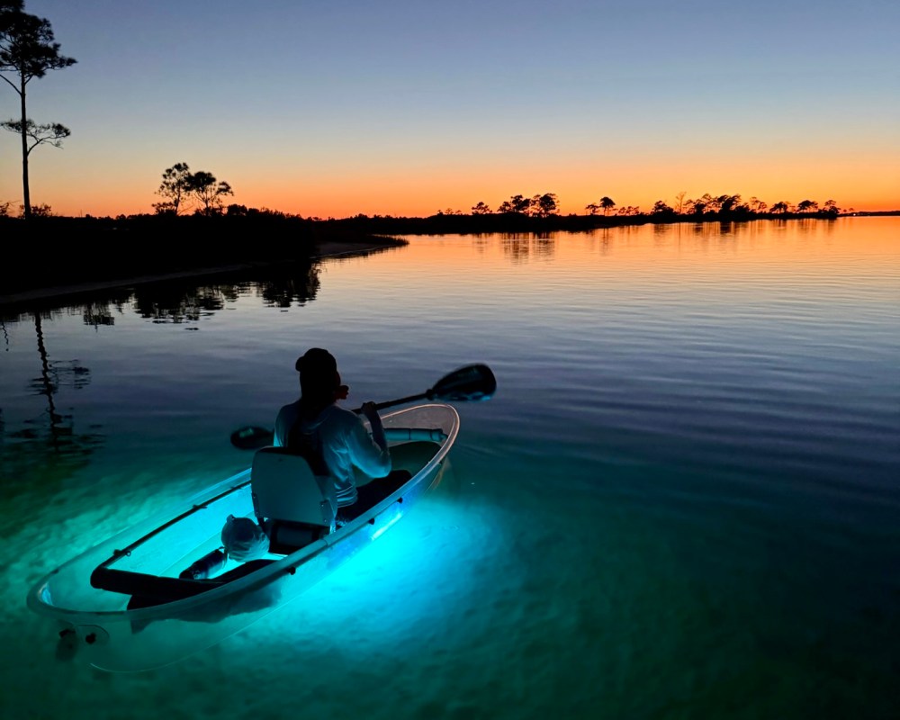 Person kayaking on calm water at sunset, kayak glowing blue.