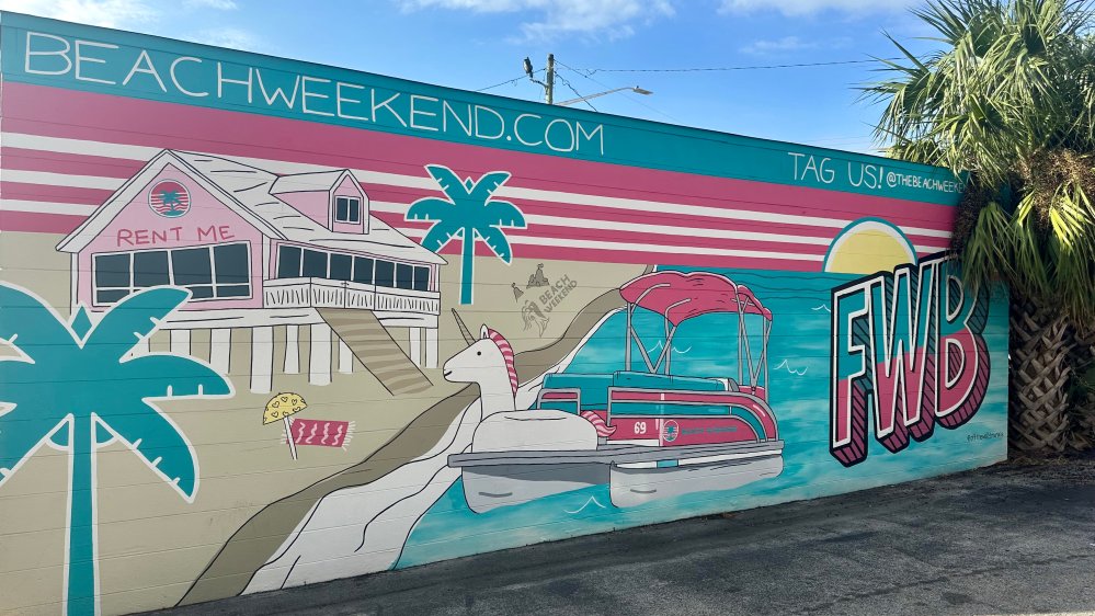 Colorful beach-themed mural with a house, palm trees, and a boat. 'BEACHWEEKEND.COM' and 'FWB' are prominently displayed.
