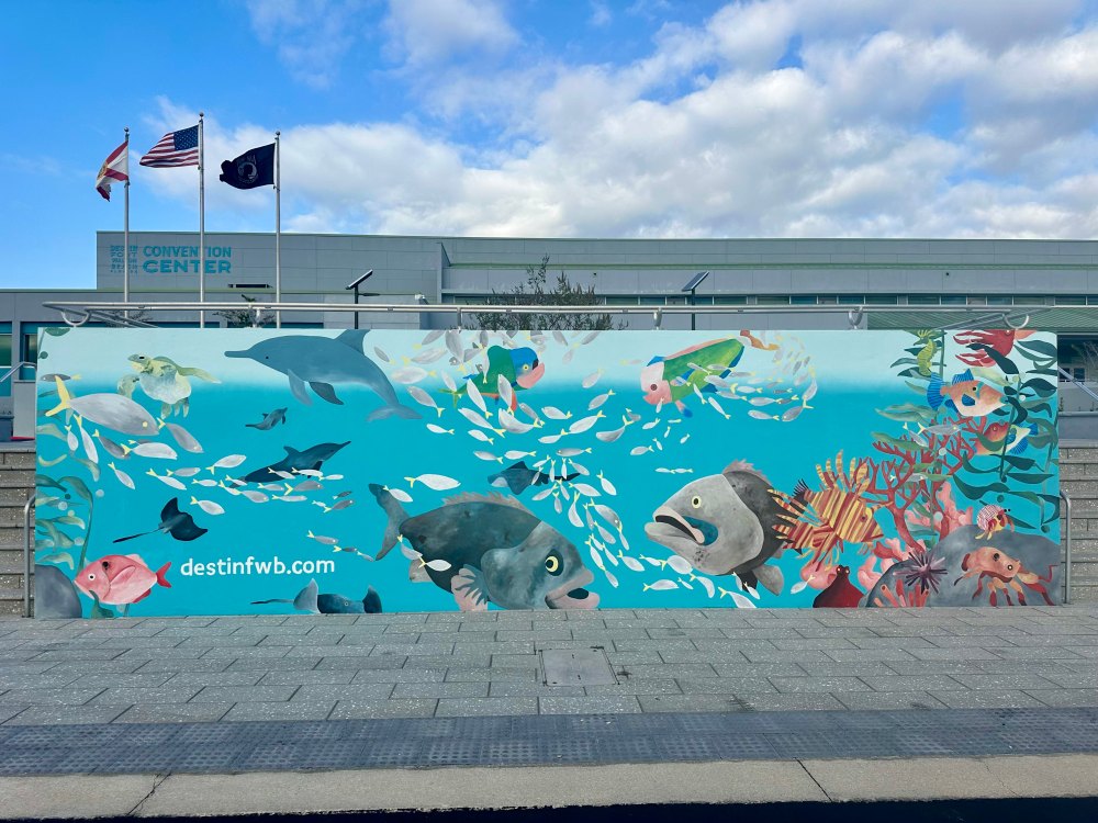 Colorful fish mural on wall at convention center with blue sky and flags in background.
