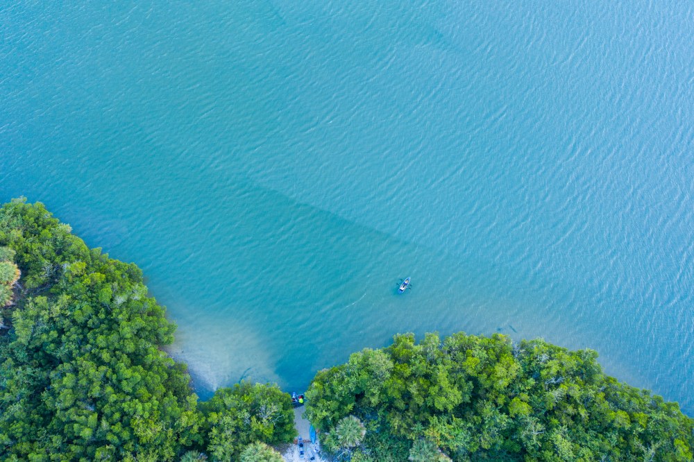 Aerial view of a small boat on a blue lake near green trees on the shoreline.
