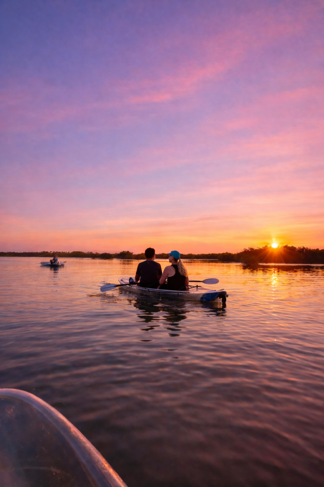 Two people kayaking on a lake at sunset with vibrant pink and orange sky.