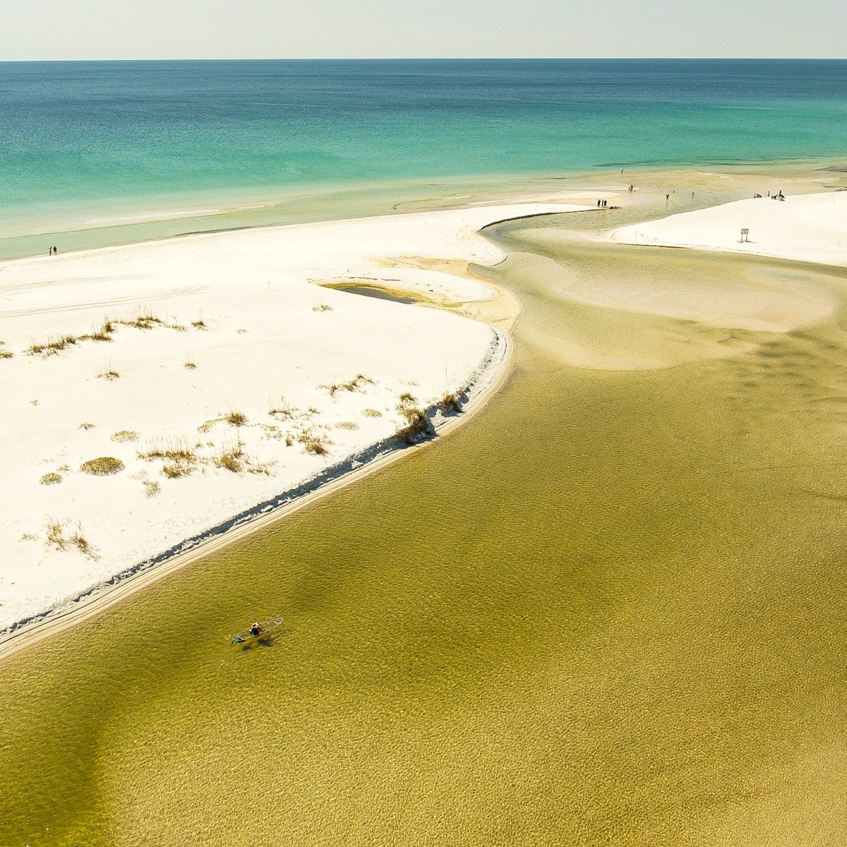 Aerial view of a sandy beach and turquoise ocean with a meandering inlet.
