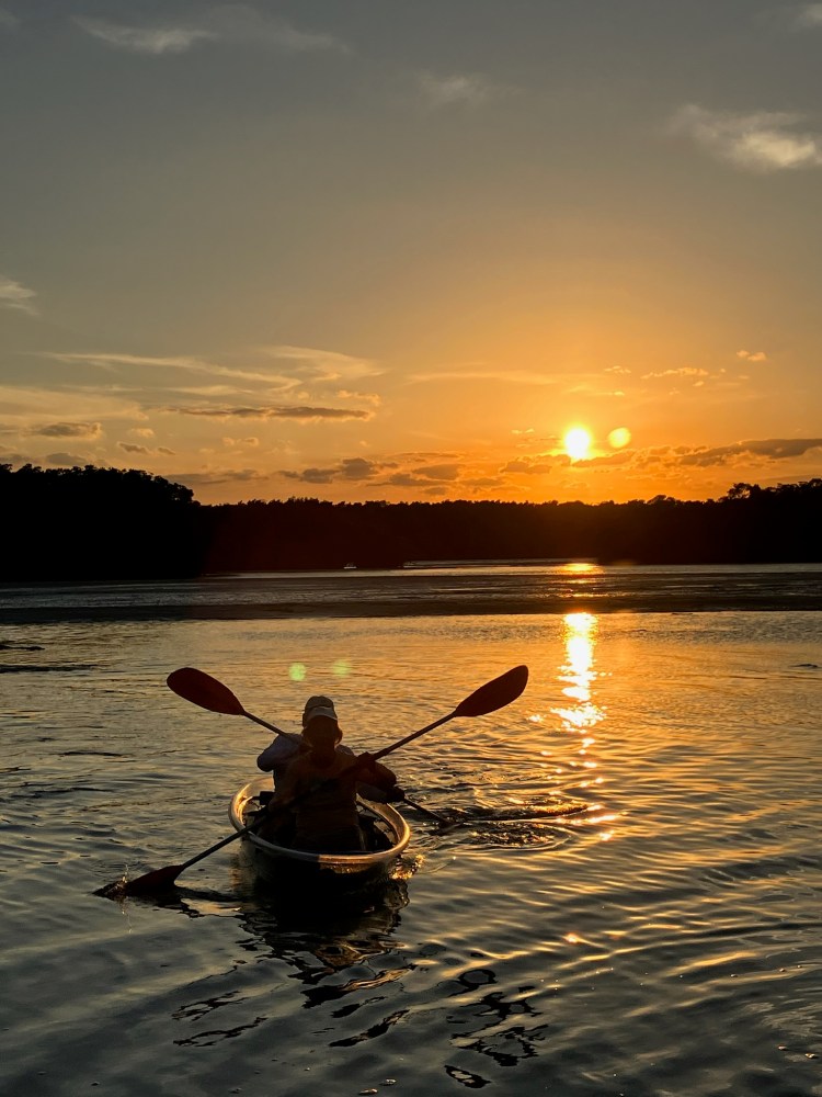 Person kayaking on a lake during a sunset with orange sky and reflections in the water.
