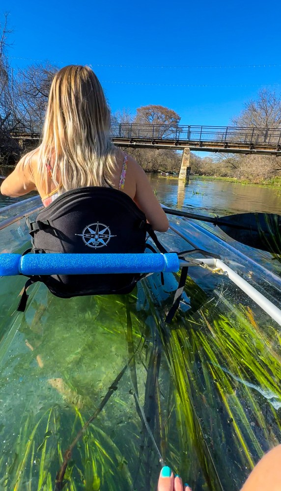 Person kayaking at night on clear water with neon lights and visible fish below.