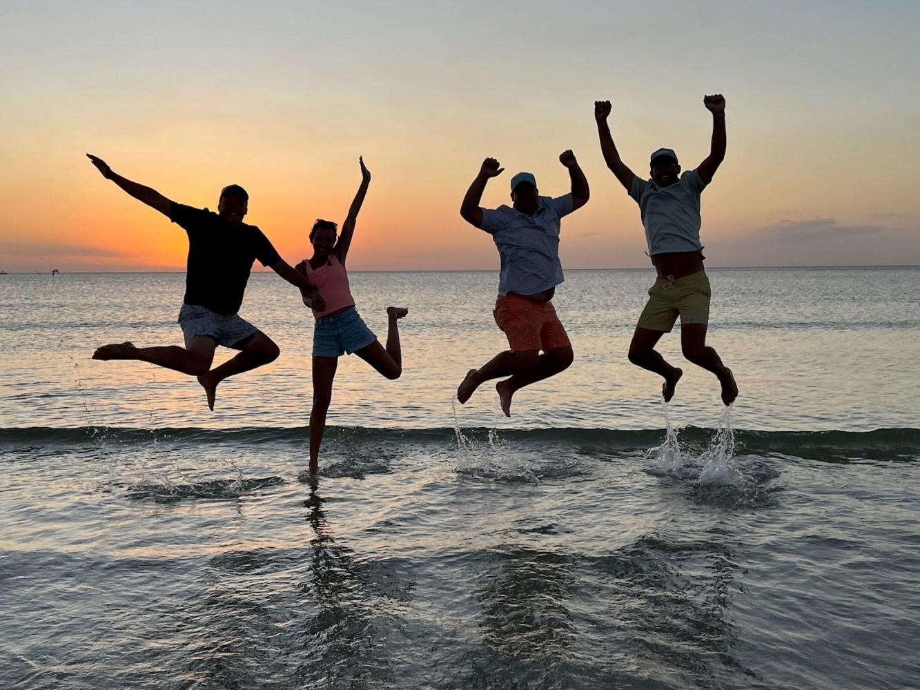 Four people jumping on a beach at sunset, silhouetted against the sky.