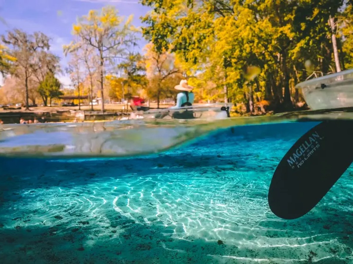 Half underwater view of a clear spring with kayaks and a paddle.