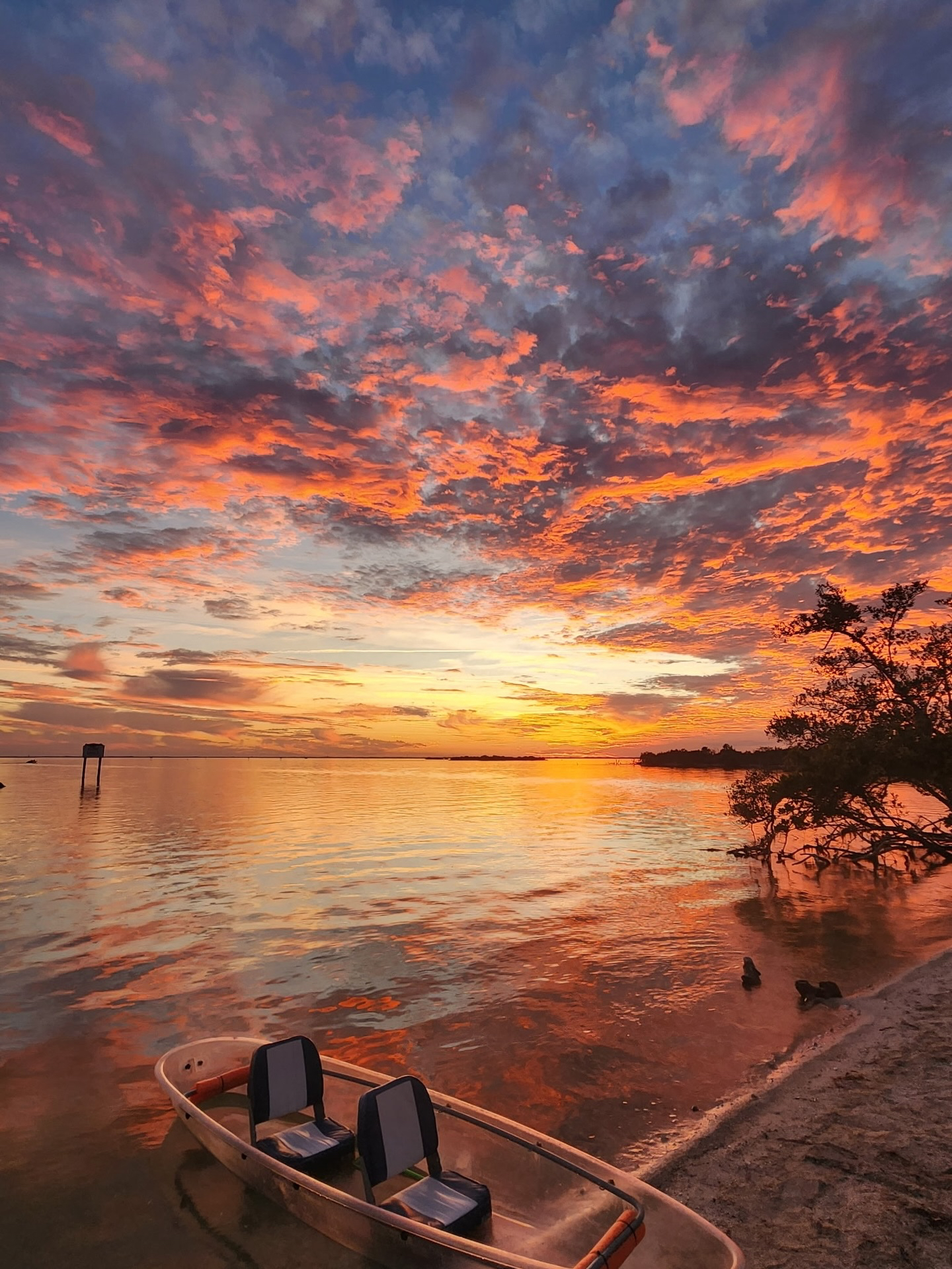 Colorful sunset over calm beach, boat on shore, dramatic clouds.