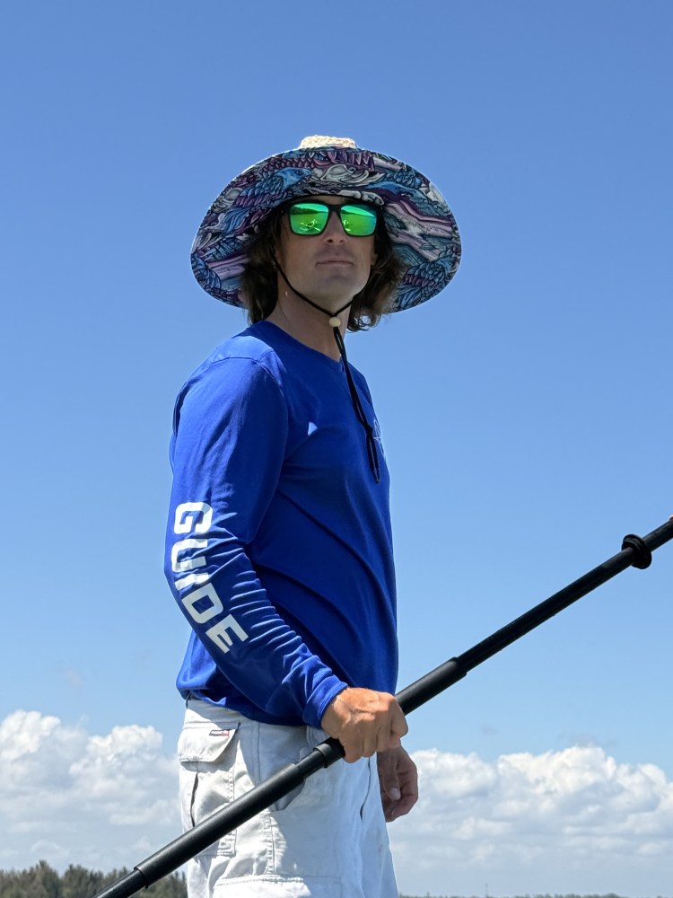 Person with wide-brim hat and sunglasses holding a paddle under clear blue sky.