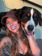 Smiling person with long hair and cap, hugging a large, happy dog.